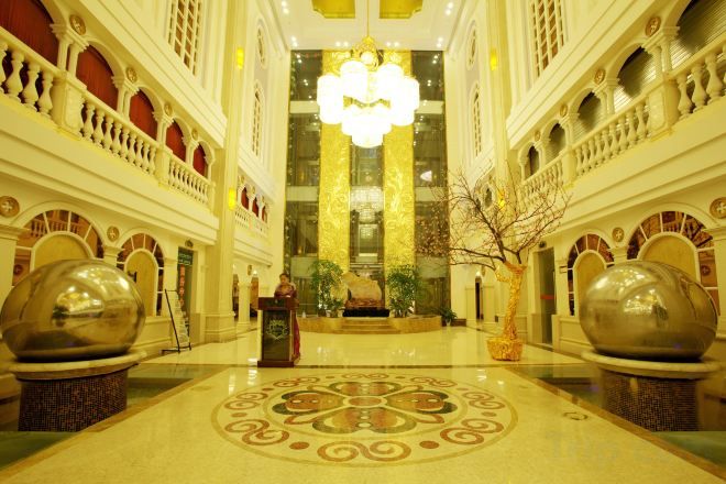 A grand lobby with a central chandelier, ornate columns, and large decorative vases.