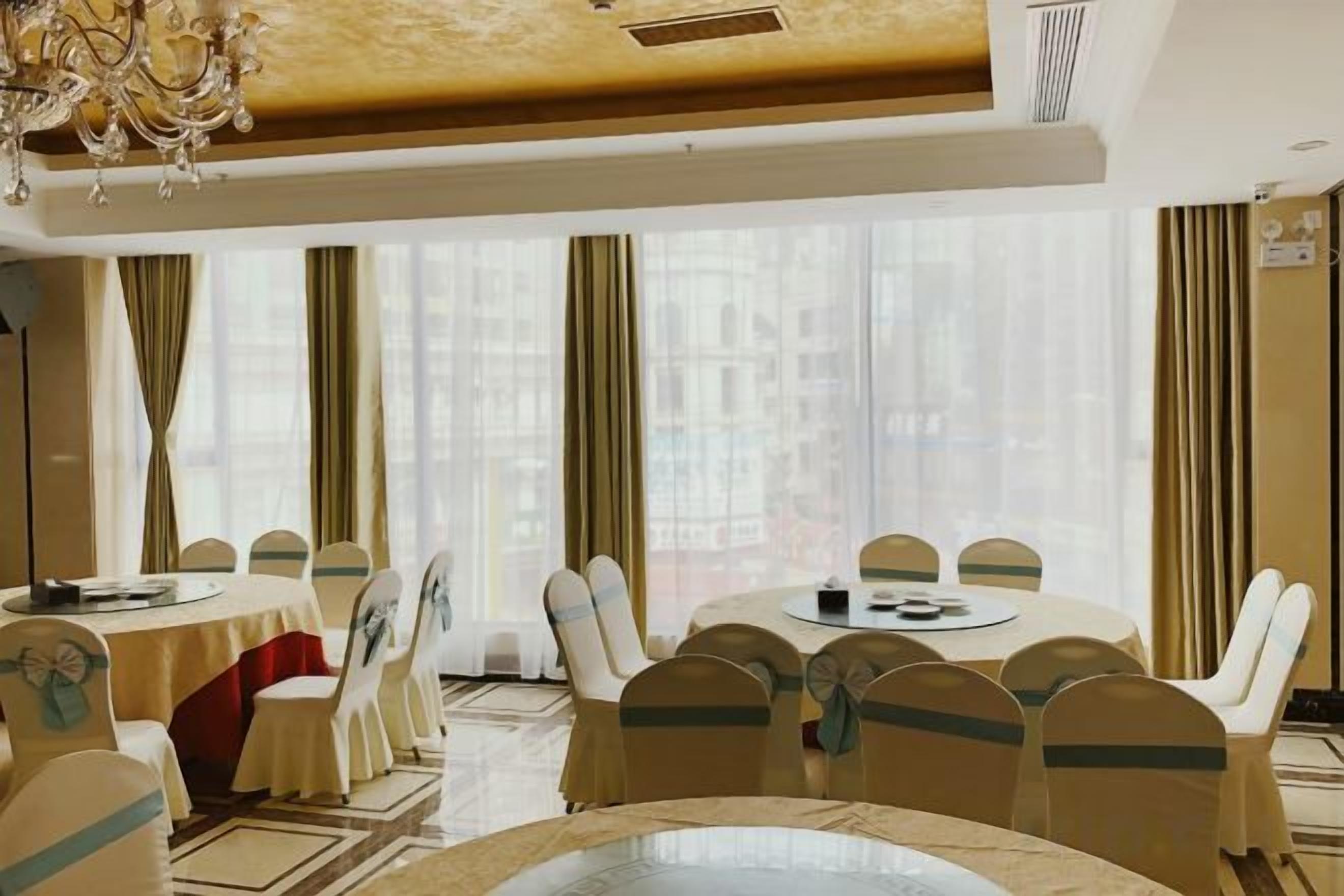 Une salle à manger d’hôtel avec des tables rondes, des chaises et un lustre.