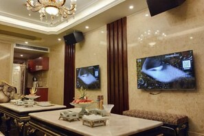 A hotel lobby with a marble reception desk, a television mounted on the wall, and a chandelier.