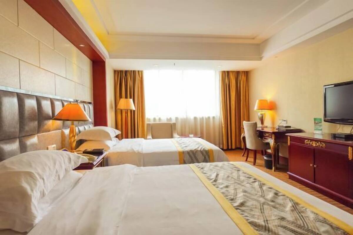 A hotel room with two beds, a desk, a television, and a window with curtains.