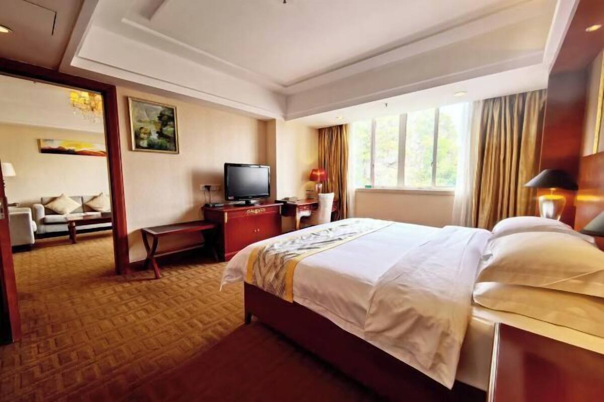 A hotel room with a bed, a desk, a television, and a window with curtains.