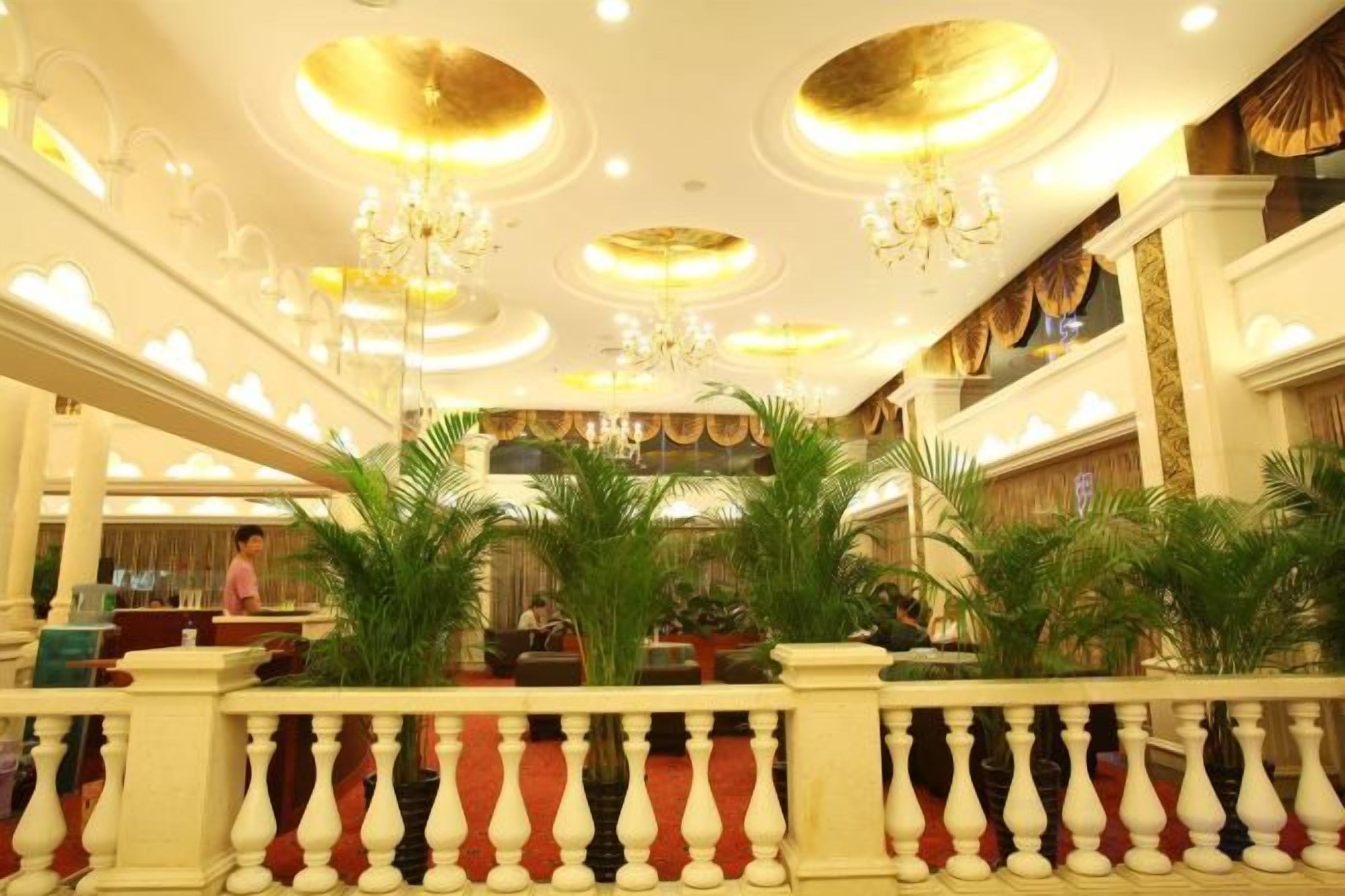Un hall d’hôtel avec un grand escalier, des lustres et des plantes en pot.