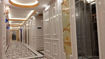 A hotel corridor with marble flooring, white paneling, and a glass elevator.