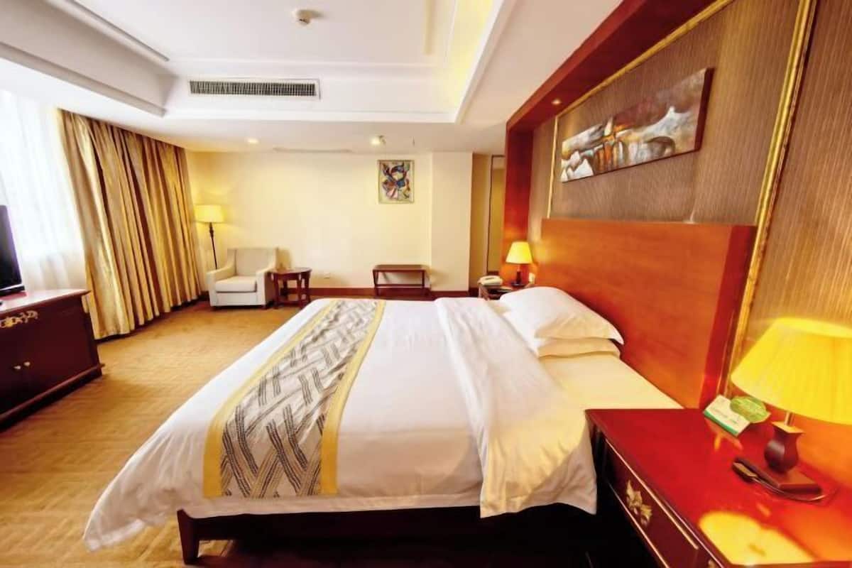 A hotel room with a bed, a desk, a chair, a TV, and a painting on the wall.