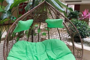 A green hanging chair with cushions in an outdoor setting with plants and a building in the background. - Riyueheng Hotel (Hezhou)