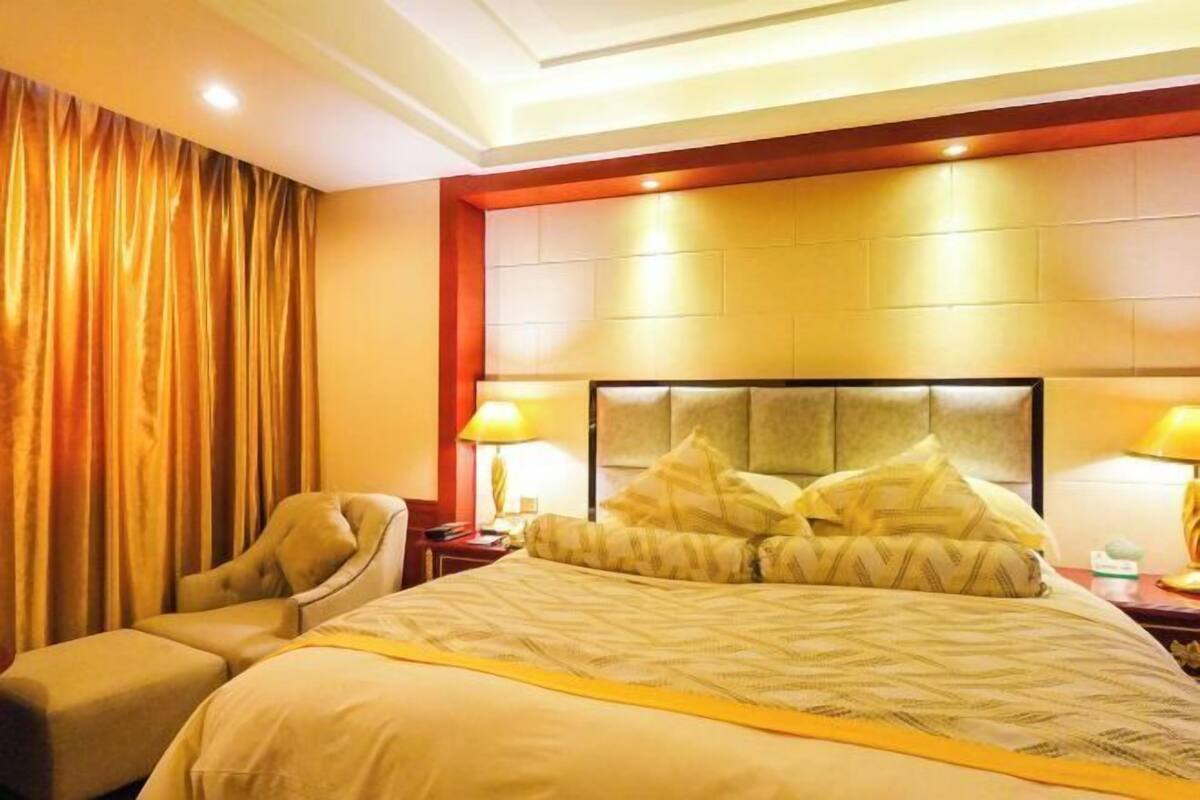 A hotel room with a large bed, a chair, a nightstand, and a headboard with built-in lighting.