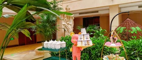 A hotel atrium with a statue, a buffet setup, and lush greenery.