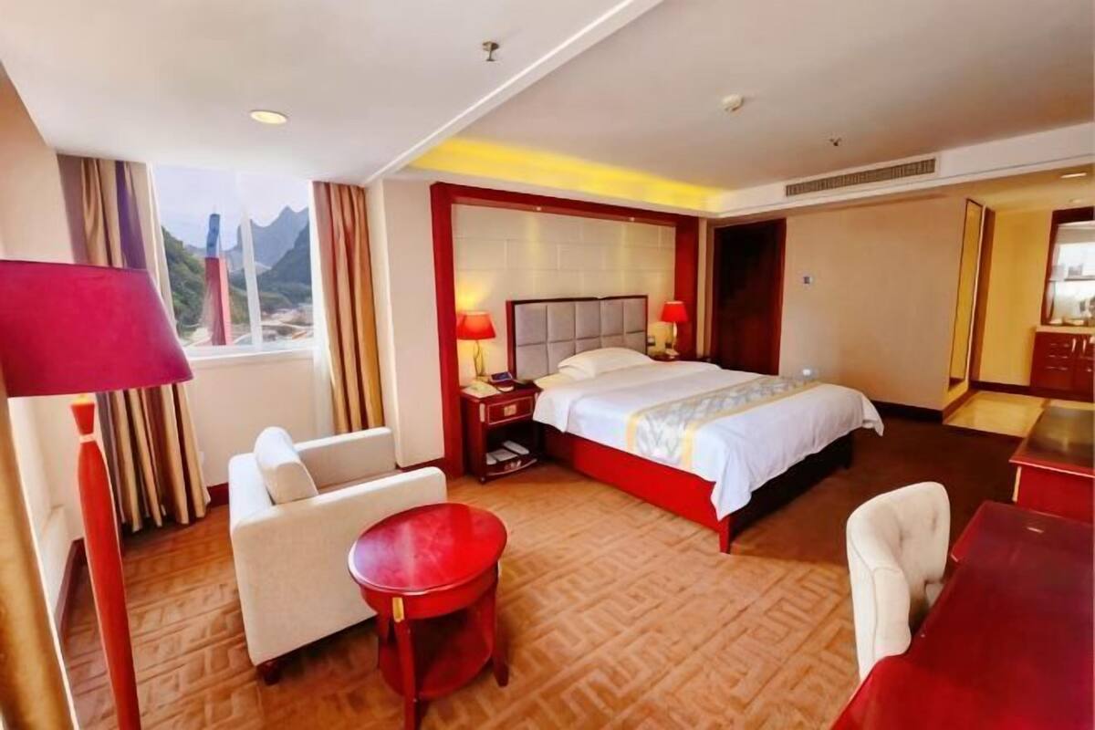 A hotel room with a bed, a desk, a chair, a small table, and a window with a view.