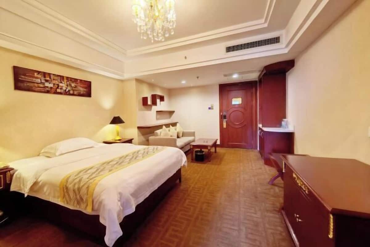 A hotel room with a bed, a desk, a chair, a dresser, and a painting on the wall.