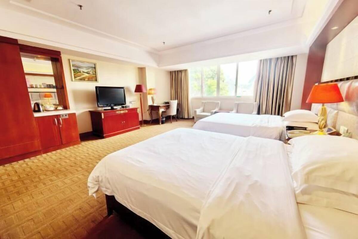 A hotel room with two beds, a TV, a desk, and a chair.