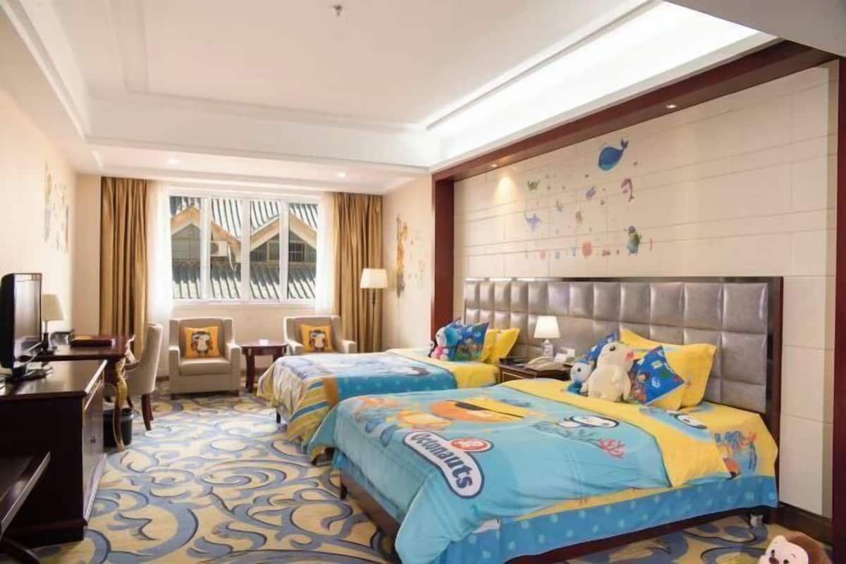 A hotel room with two beds, a desk, a chair, a television, and a window with curtains.