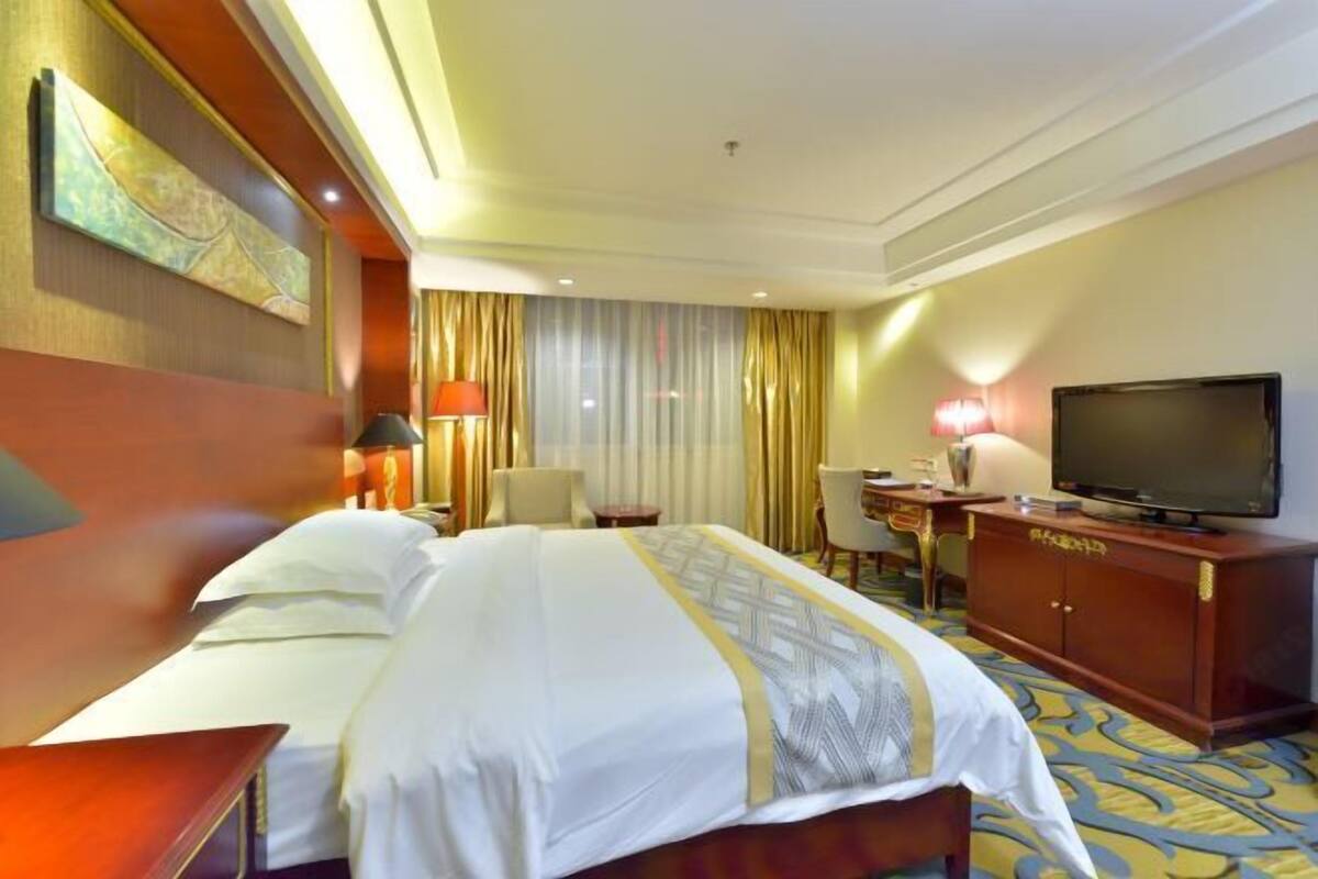 A hotel room with a large bed, a desk, a television, and a chair.