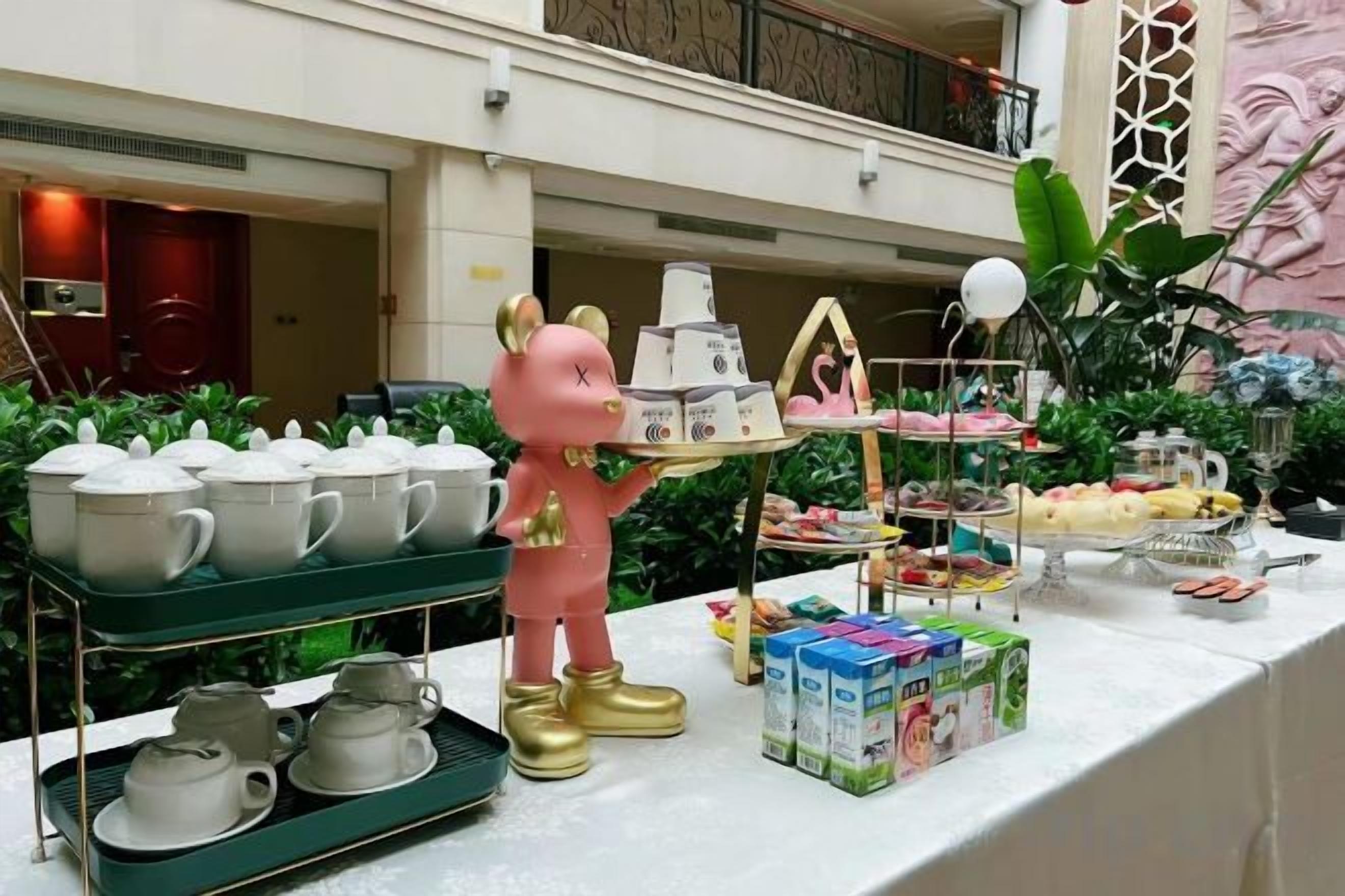 A buffet setup with tea sets, a decorative pig figure, and various food items.