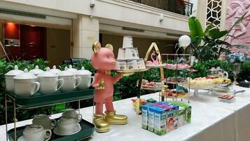 A buffet setup with tea sets, a decorative pig figure, and various food items.