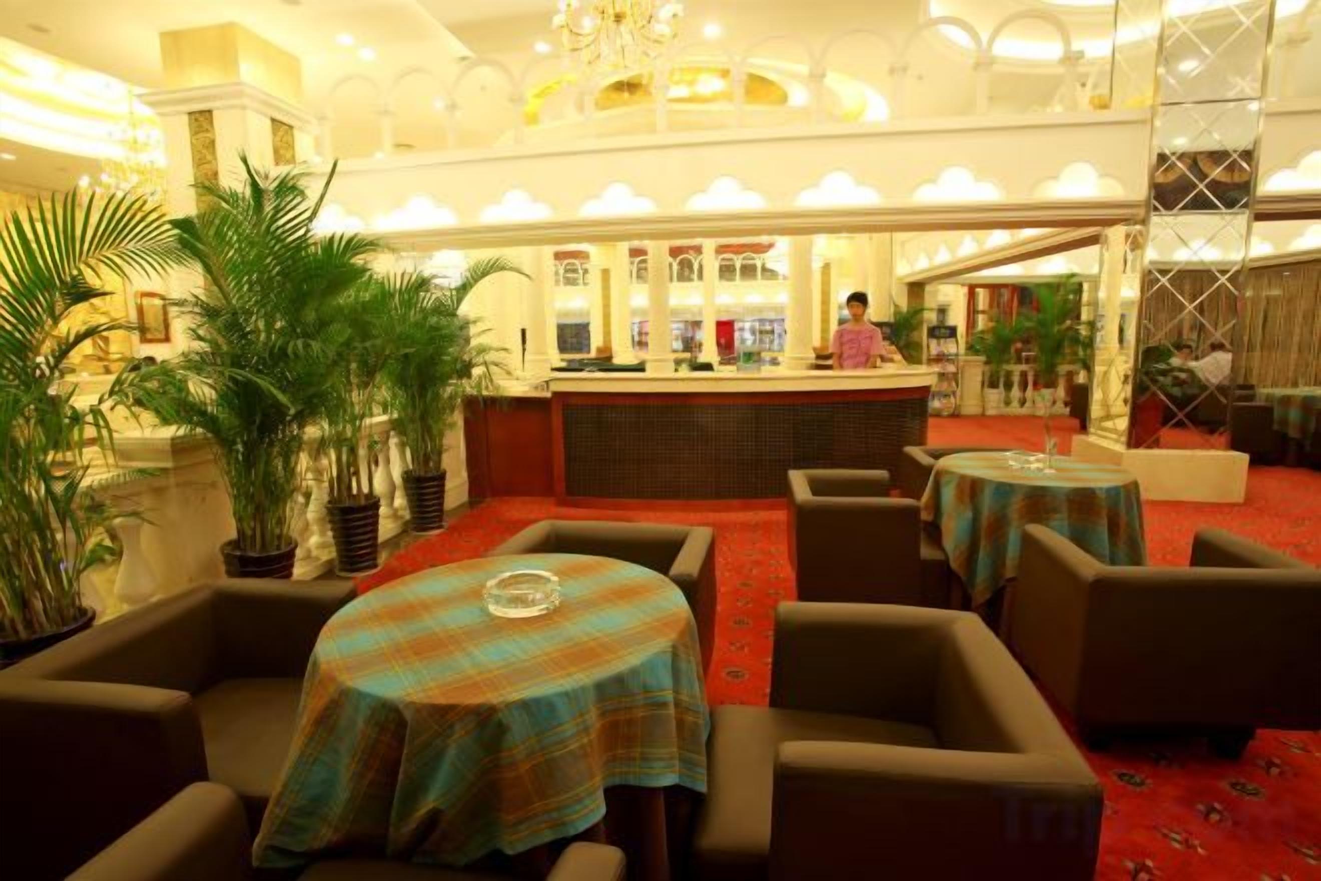 A hotel lobby with a reception desk, seating area, and potted plants.