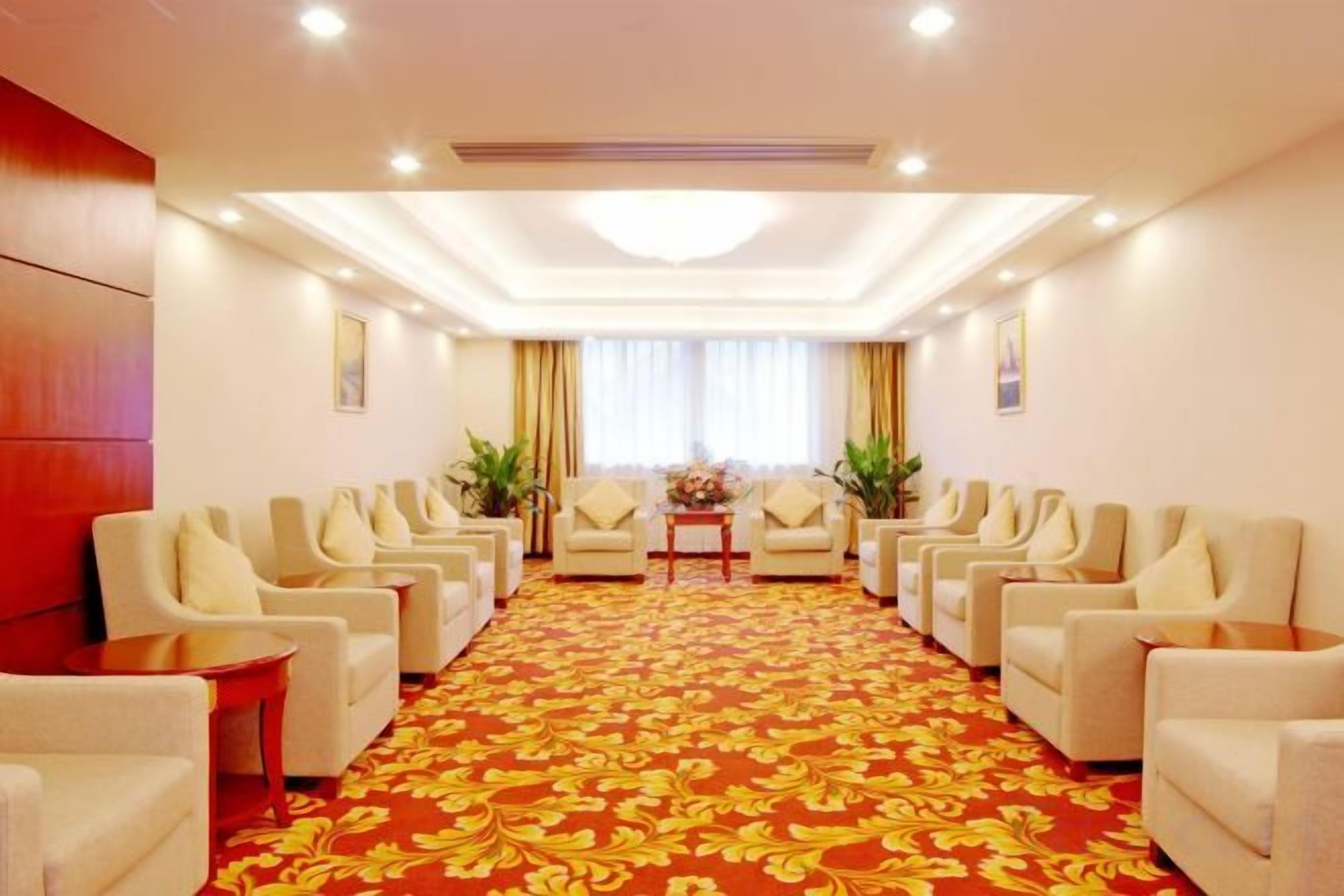 Un salón de conferencias de hotel con filas de sillas, una alfombra roja y un amplio ventanal con cortinas.