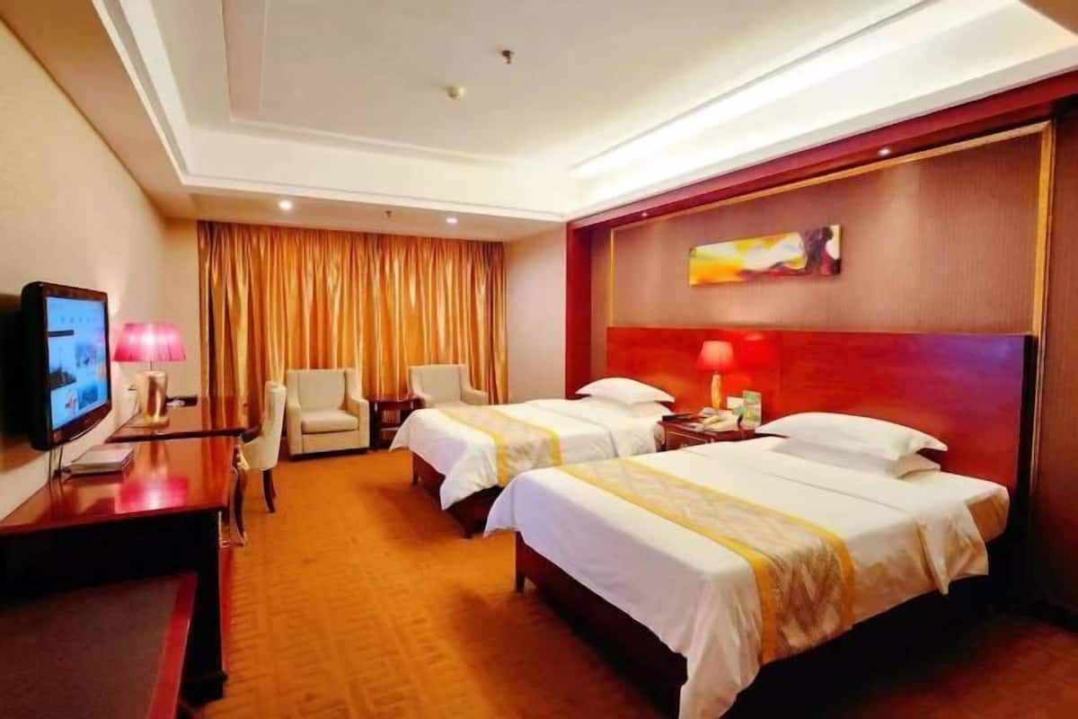 A hotel room with two beds, a desk with a TV, a chair, and a painting on the wall.