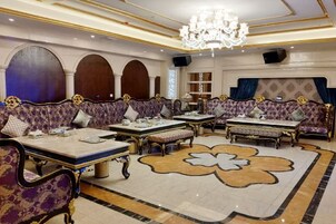 Un lobby de hotel lujoso con sofás ornamentados, una alfombra floral grande y un candelabro.