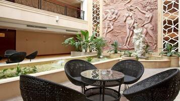 A courtyard with wicker chairs, a glass table, and a decorative wall with a relief sculpture.
