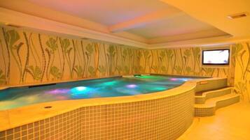 A hot tub with a tiled surround and a television screen mounted on the wall.