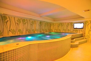 A hot tub with a tiled surround and a television screen mounted on the wall. - Riyueheng Hotel (Hezhou)