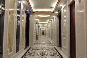 Um corredor comprido e estreito, com piso de mármore e portas em ambos os lados.