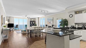 A spacious living area with a large island, a dining table, and a view of the ocean. - Gulf-front PCB Condo w/ Balcony, Resort Amenities, Game Room, Pools & Beach Gear Tortuga 1301 by Avantstay (Panama City Beach)