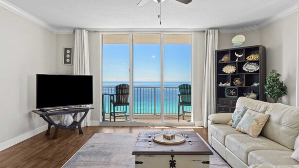 A living room with a television, a coffee table, a sofa, and a view of the ocean through large sliding doors. - Gulf-front PCB Condo w/ Balcony, Resort Amenities, Game Room, Pools & Beach Gear Tortuga 1301 by Avantstay (Panama City Beach)