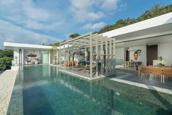 Une maison moderne dotée d’une grande piscine, d’un espace salon extérieur et d’un coin repas.