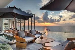 Une chambre moderne avec un mur de verre donnant sur l’océan au coucher du soleil.