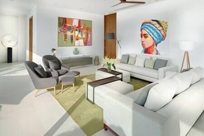Un salon moderne avec un canapé blanc, des fauteuils gris et une table basse. Un tableau orne le mur et une lampe sur pied se trouve dans un coin.