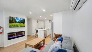 Ett modernt vardagsrum med en platt-TV, en öppen spis, en soffa och ett kök i bakgrunden.