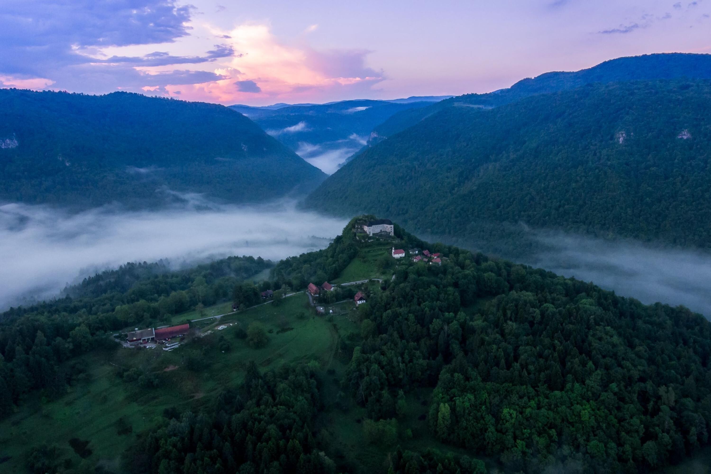Un paisaje montañoso con un valle y un pequeño grupo de edificios en una colina.