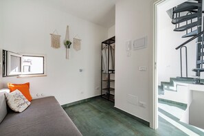 Una habitación moderna con un sofá gris, un colgador de macramé y una escalera que lleva a un piso superior.