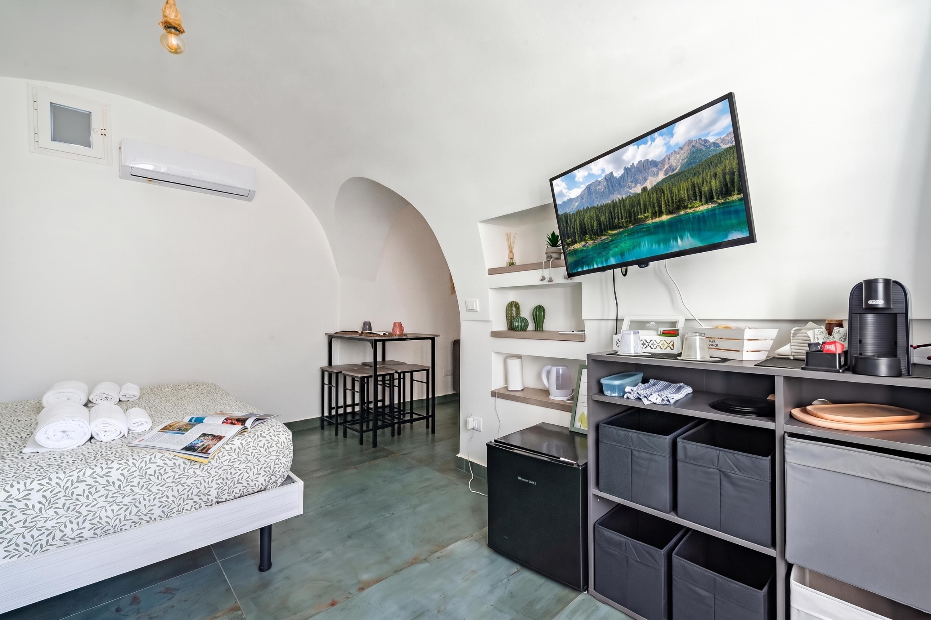 A compact hotel room with a bed, a desk, a television, and storage bins.
