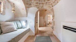 Un corridoio stretto con soffitto in pietra, un divano con cuscini a righe e un tappeto decorato.