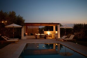 An outdoor pool area with lounge chairs, umbrellas, and a barbecue setup. - Masseria Maranna Trulli&Spa Luxury Villa, Martina Franca, Italy (Martina Franca)