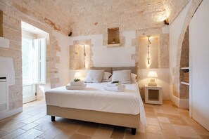 A bedroom with a large bed, two bedside tables with lamps, a stone wall, and a window. - Masseria Maranna Trulli&Spa Luxury Villa, Martina Franca, Italy (Martina Franca)