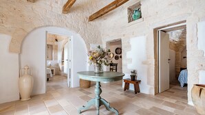 Un interno rustico con un tavolo rotondo, pareti in pietra e una porta che conduce in un'altra stanza.
