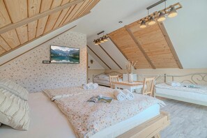Una camera da letto con soffitto spiovente, un letto con copriletto floreale, un comodino con una lampada e una TV a parete che mostra un paesaggio montano.