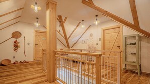 A wooden interior with a high ceiling, exposed beams, and a wooden railing. There are hanging lights and a small cabinet with glass doors.