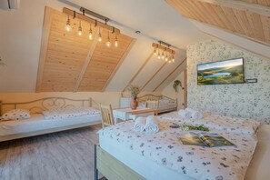 Un dormitorio con techo inclinado, una cama con ropa de cama floral, una mesita de noche con un jarrón y un televisor montado en la pared.