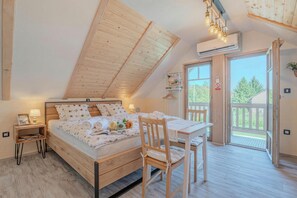 Een slaapkamer met een schuine kap, een bed, een tafel met een stoel en een balkon met uitzicht.
