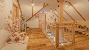 A cozy attic bedroom with wooden beams, a crib, a sofa, and a decorative wall.