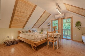 Een slaapkamer met een houten bed, een bureau en een stoel. Er is een raam met uitzicht op groen.