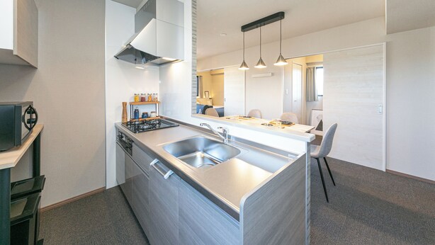 Une cuisine moderne dotée d’une cuisinière intégrée, d’un évier et d’une hotte aspirante. On y trouve également un coin repas avec une chaise et un luminaire suspendu.