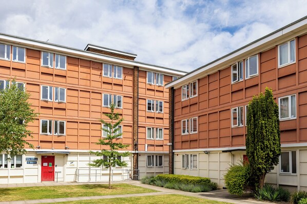 Un immeuble résidentiel à plusieurs étages, avec une porte rouge, des fenêtres à cadre blanc et une façade en briques.