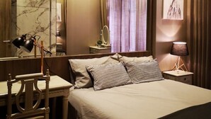 A hotel room with a large bed, a desk with a chair, a mirror, a lamp, and a painting on the wall. - Mayfair Bangkok (Krung Thep Maha Nakhon)
