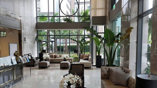 A spacious lobby with a high ceiling, large windows, and a central seating area with sofas and a coffee table. - Mayfair Bangkok (Krung Thep Maha Nakhon)