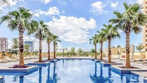 Una piscina con palmeras, sillas de descanso y un paisaje urbano al fondo.